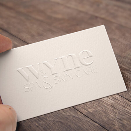 Hand holding the embossed business card featuring the Wyne spa and skin care new rebranded logo.